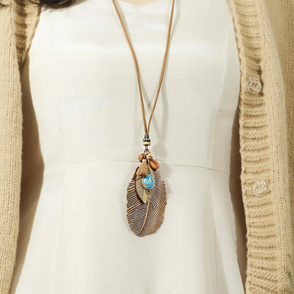 Necklace with feather and blue stone pendant worn by a person in a beige cardigan.