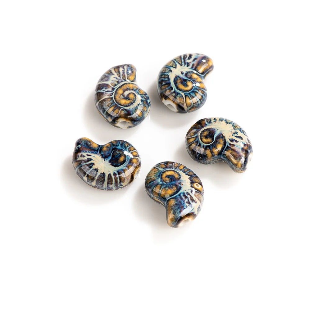 Five ceramic beads shaped like nautilus shells, featuring a glossy glaze with blue, gold, and cream patterns, arranged on a white background.