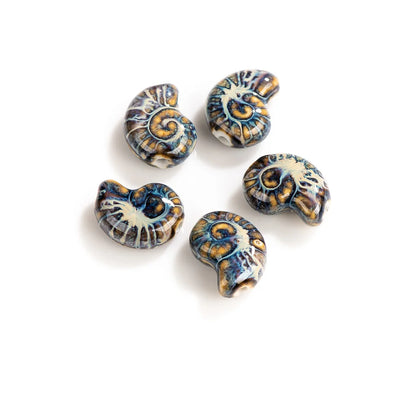 Five ceramic beads shaped like nautilus shells, featuring a glossy glaze with blue, gold, and cream patterns, arranged on a white background.