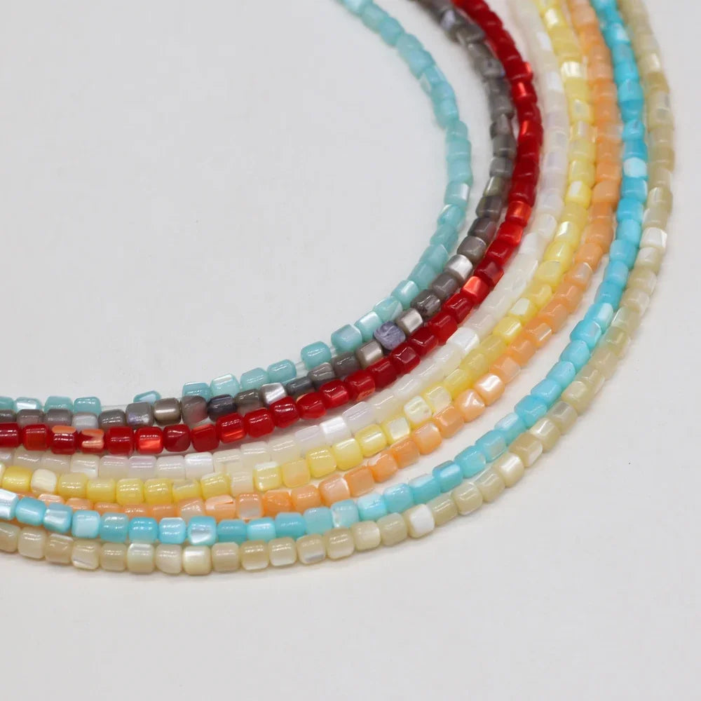 Six strands of small rectangular faceted shell beads arranged in overlapping curved rows on a plain white background. The beads come in red, gray, turquoise blue, pale yellow, peach, and cream colors.