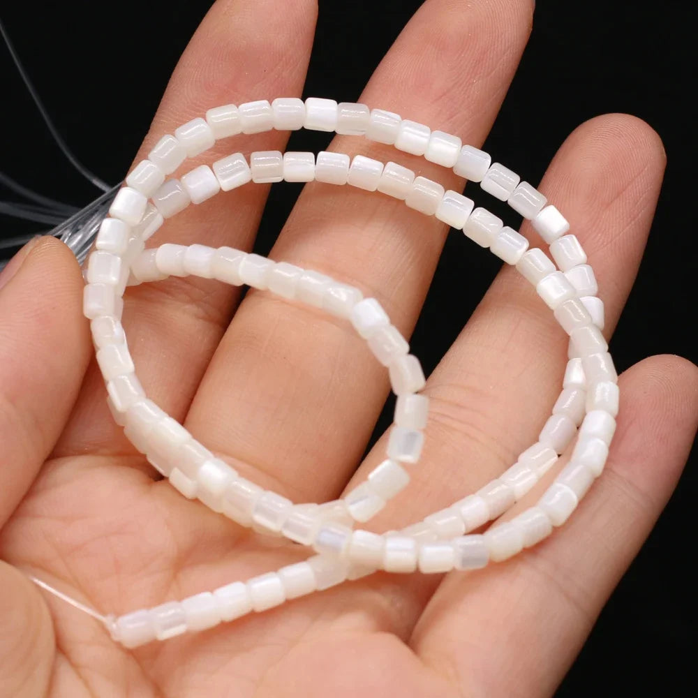 White rectangular faceted shell beads strung on a clear cord, coiled and held in a person's hand against a black background.