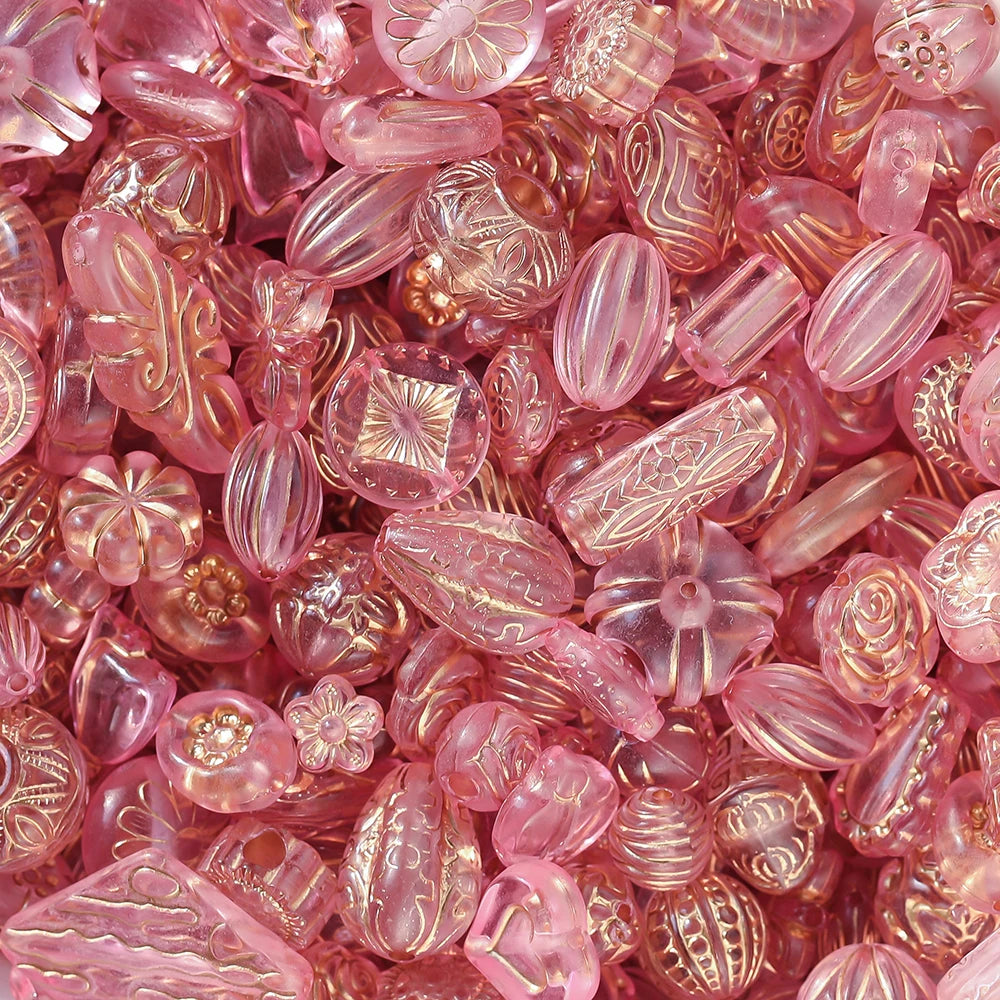 A dense pile of pink translucent glass beads in various shapes and patterns, including floral, striped, and textured designs.