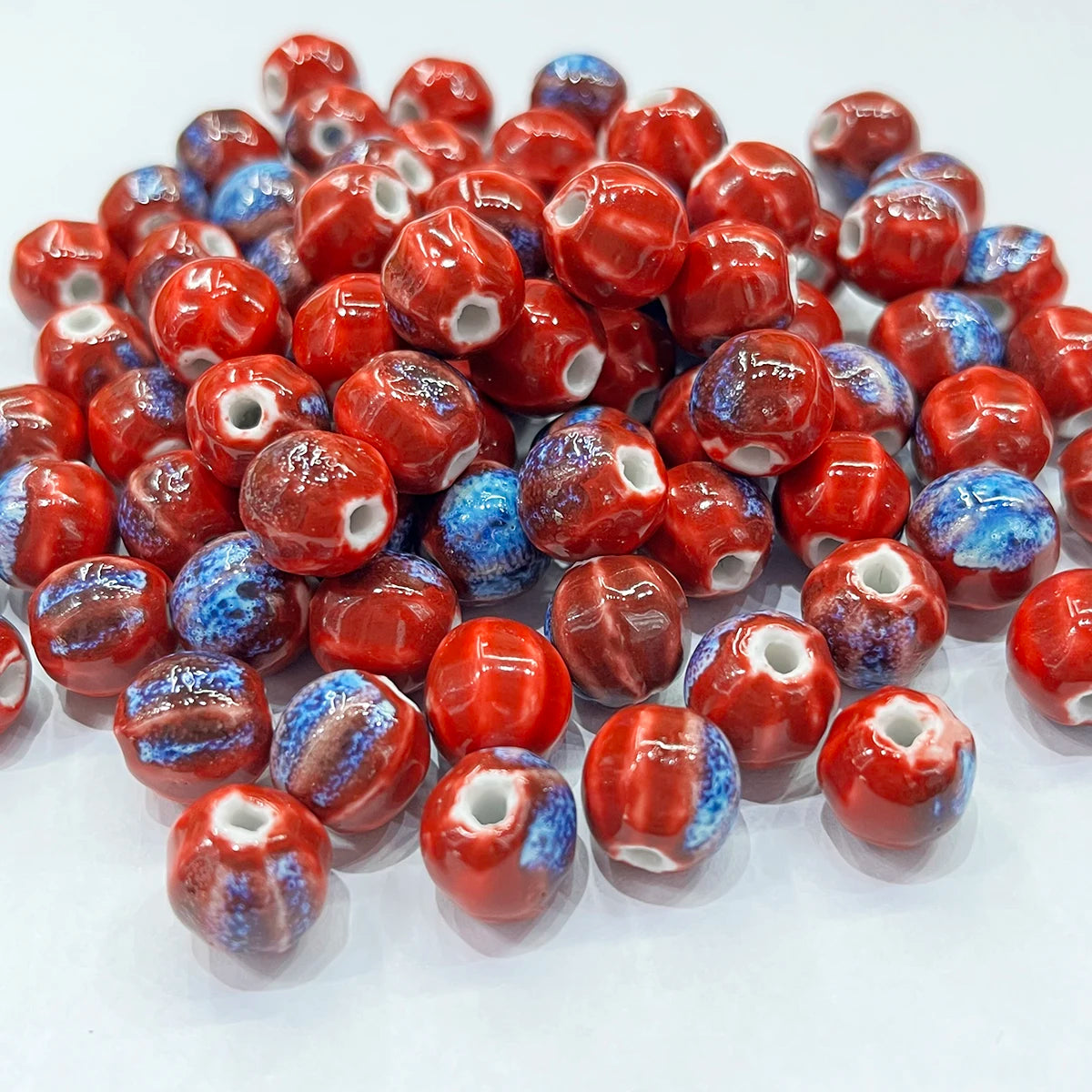 A pile of round ceramic beads with a glossy red and blue marbled pattern, featuring a white opening in the center of each bead, set against a plain white background.
