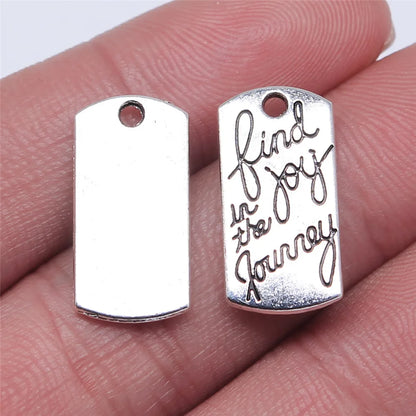 Silver pendant with 'find joy in the journey' engraving held between fingers.
