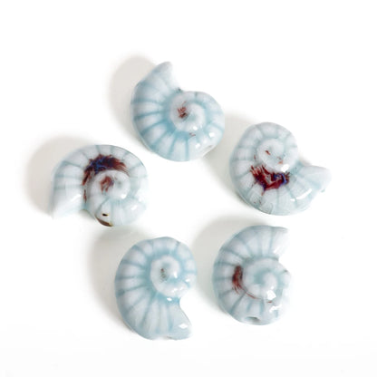 Five glossy ceramic nautilus shell beads in light blue and white with dark brown accents, arranged on a plain white background.