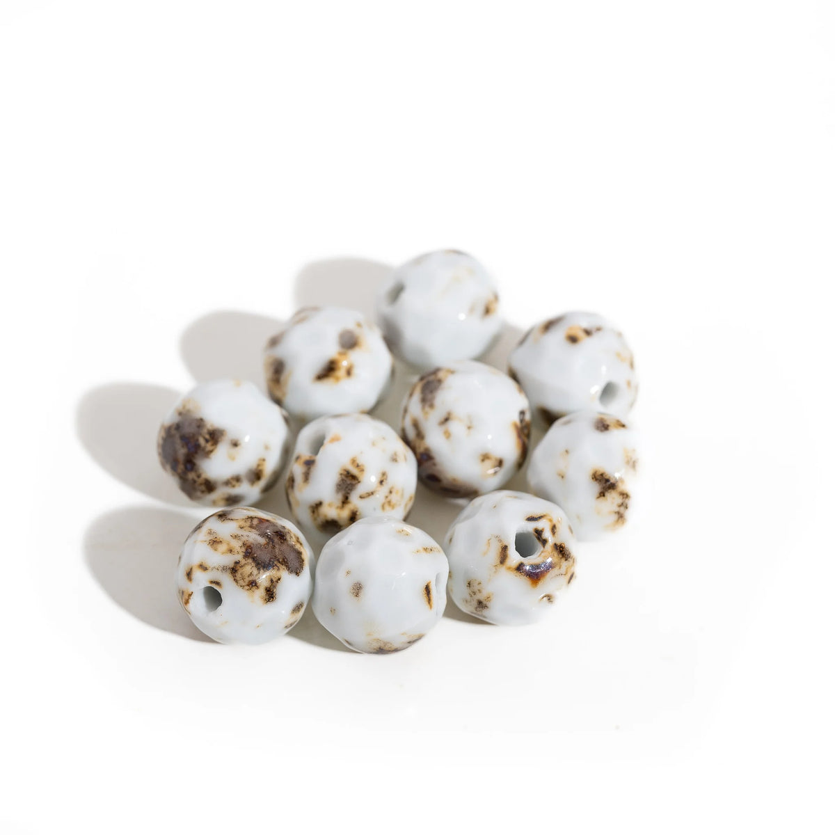 A cluster of handmade ceramic beads with a white base and dark brown mottled speckles, arranged on a plain white background.