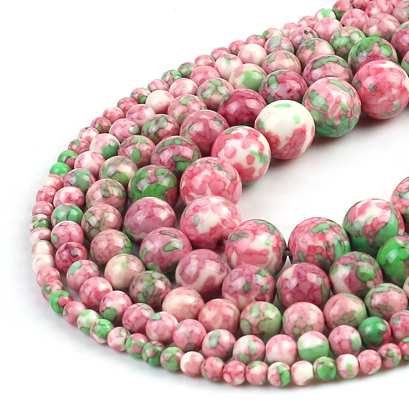 Curled strands of round gemstone beads in pink, white, and green marbled patterns on a white background.