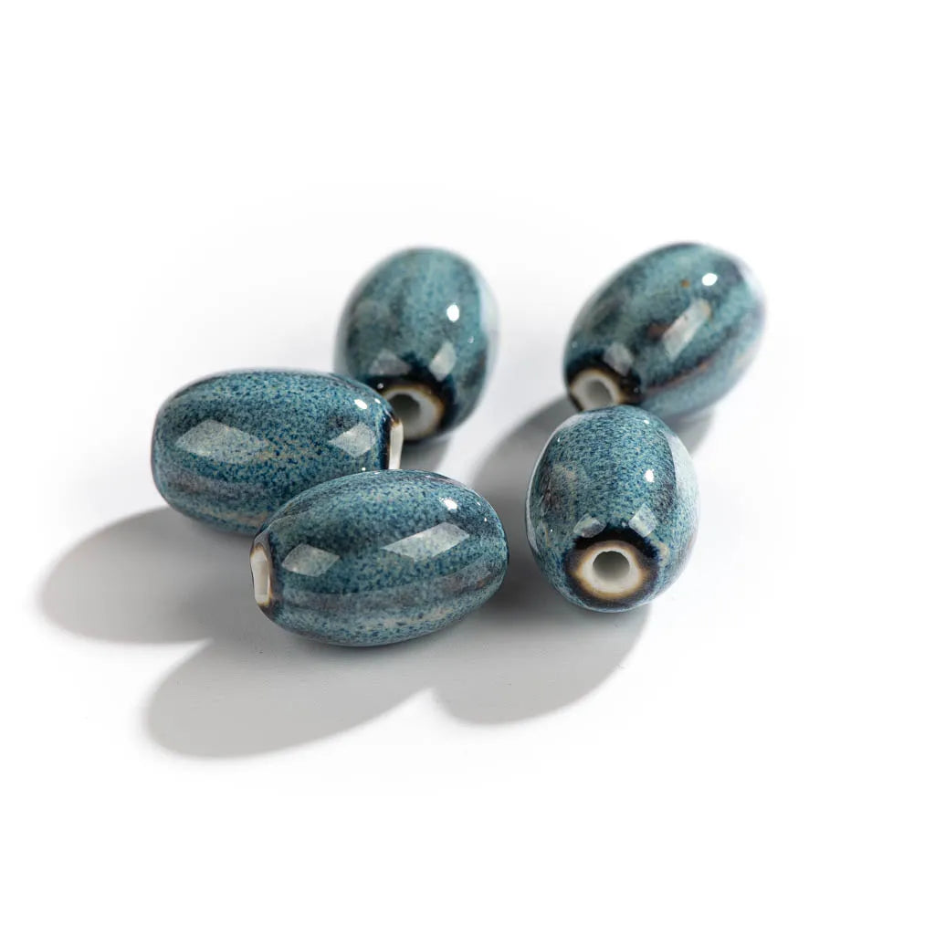 Four glossy, oval-shaped ceramic beads in a speckled teal blue and white glaze, arranged on a clean white background with soft shadows.