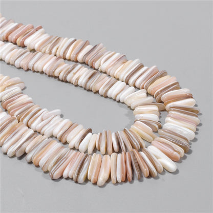 A strand of elongated mother of pearl shell beads in natural beige, cream, and light brown tones, arranged in a loose curve on a neutral gray background.