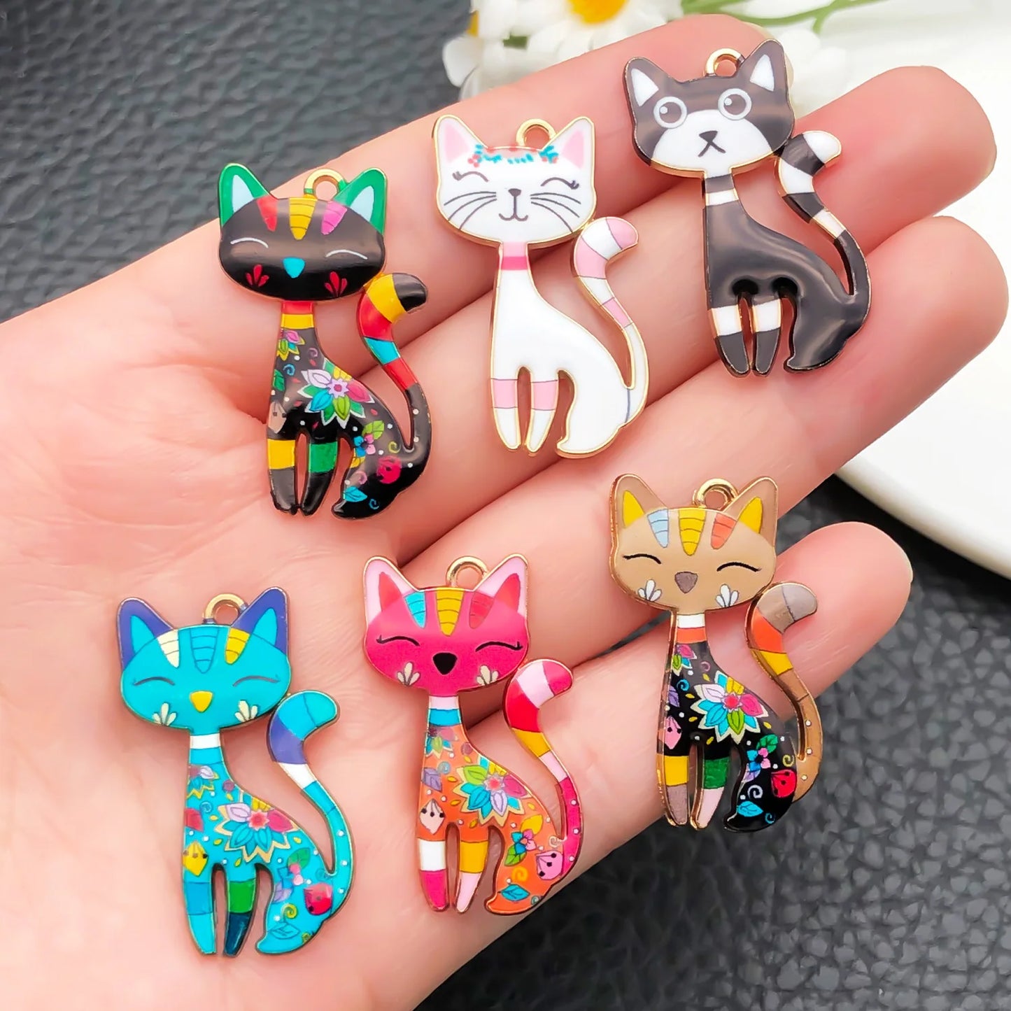 Colorful cat-shaped charms on a hand against a dark textured background
