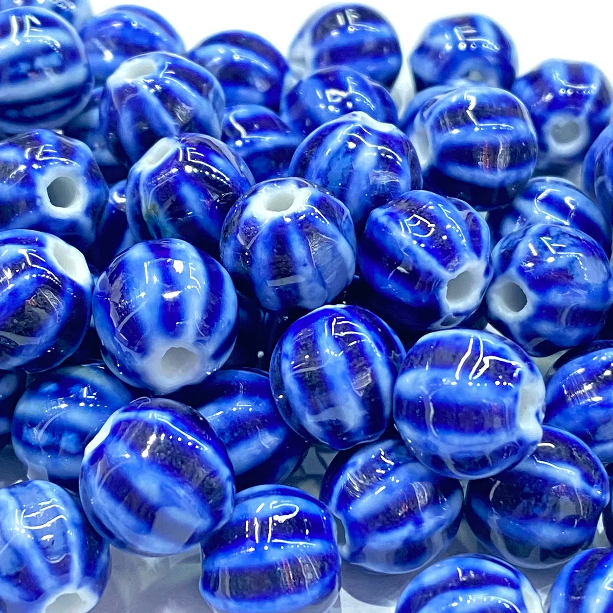 A pile of glossy blue and white marbled glass beads with a central hole, shown in a close-up view on a white background.