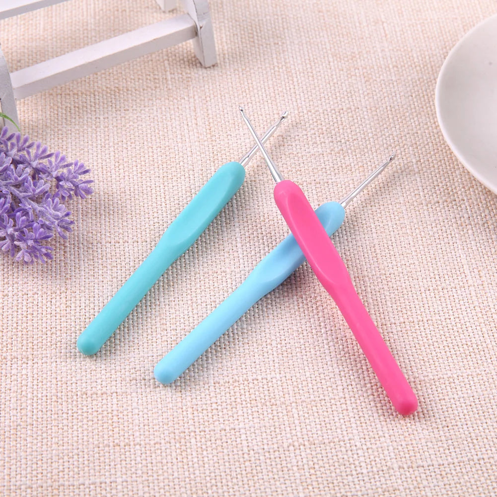 Two crochet hooks, one pink and one blue, on a textured surface with lavender flowers.