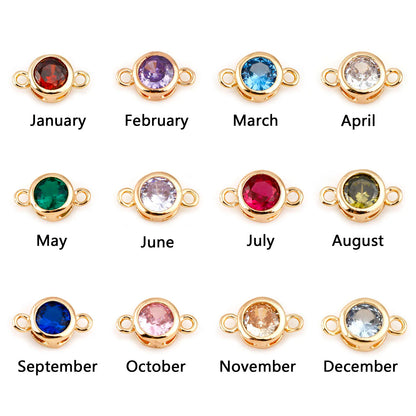 Twelve gold-toned round bezel settings with small side loops, each labeled January through December, shown on a white background. The stones change color monthly: red, purple, blue, clear/white, green, pale lavender, pink, olive green, dark blue, pale pink, peach, and light blue.