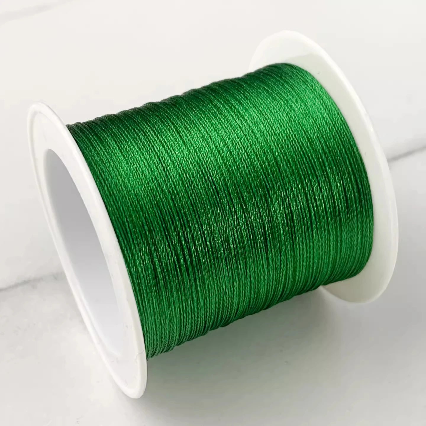 A spool of vibrant green embroidery thread wound tightly on a white plastic core, photographed on a light gray surface.