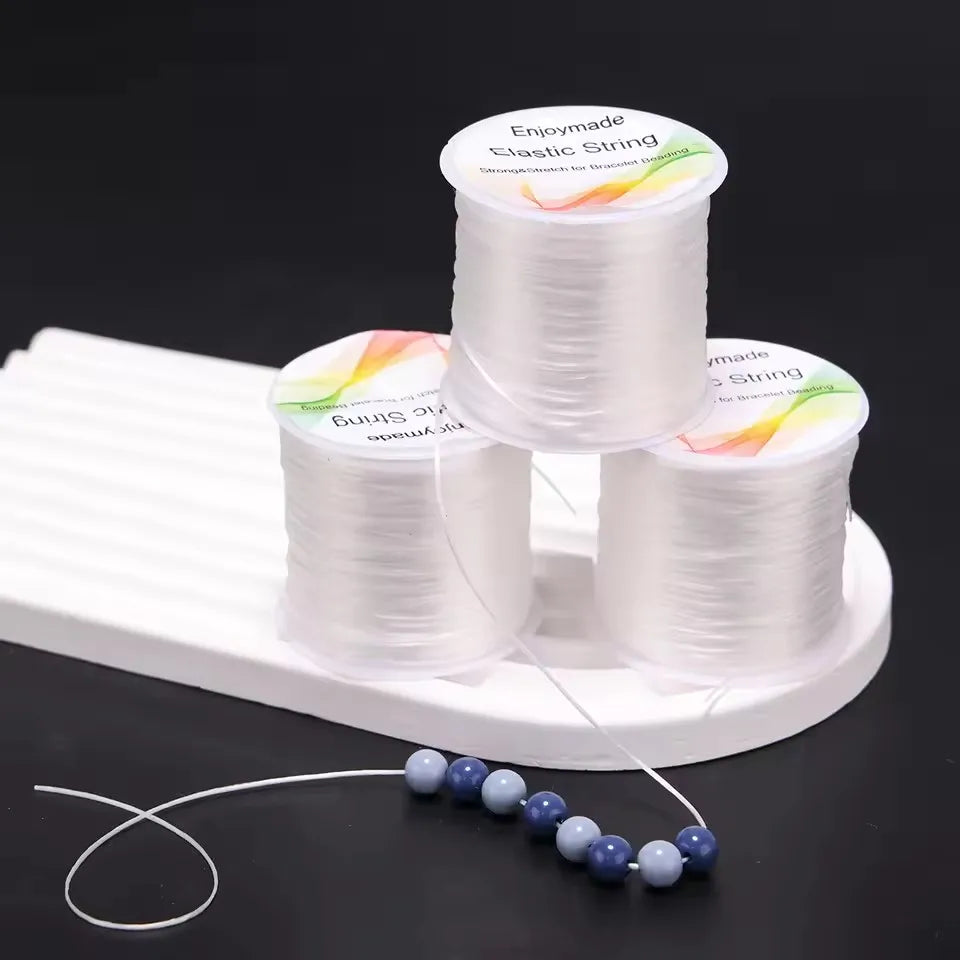 Three spools of white elastic string with a beaded necklace on a black background