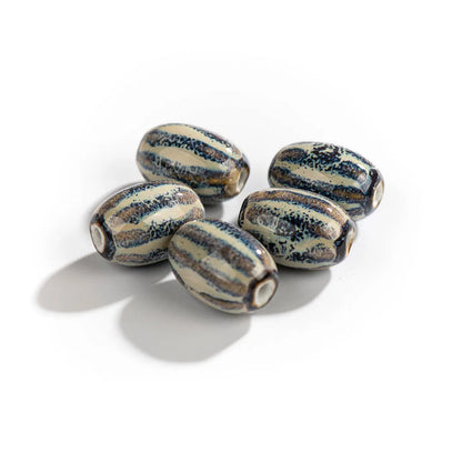 Five handmade ceramic beads with a striped pattern of dark blue, black, and cream, arranged on a white background with soft shadows.