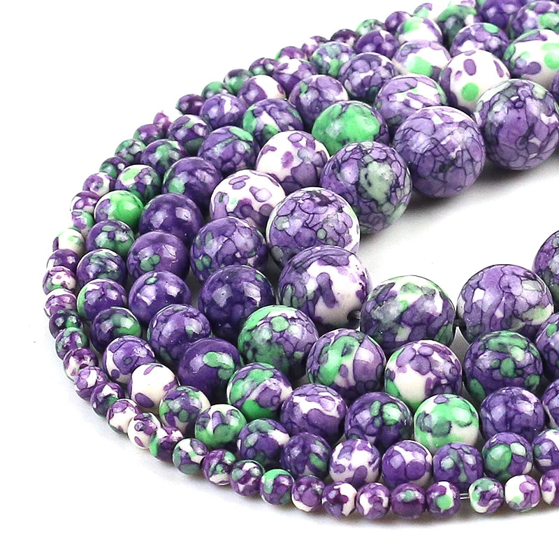 Multiple strands of polished round beads in a marbled pattern of purple, green, and white, arranged in a curve on a white background.