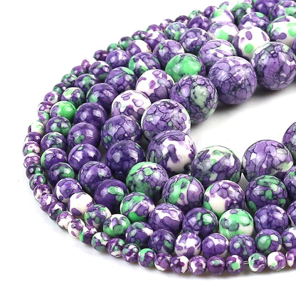 Multiple strands of polished round beads in a marbled pattern of purple, green, and white, arranged in a curve on a white background.