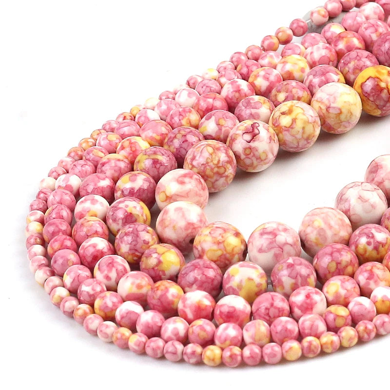 Multiple strands of round gemstone beads in pink, white, and yellow marbled patterns, arranged in a spiral on a white background.