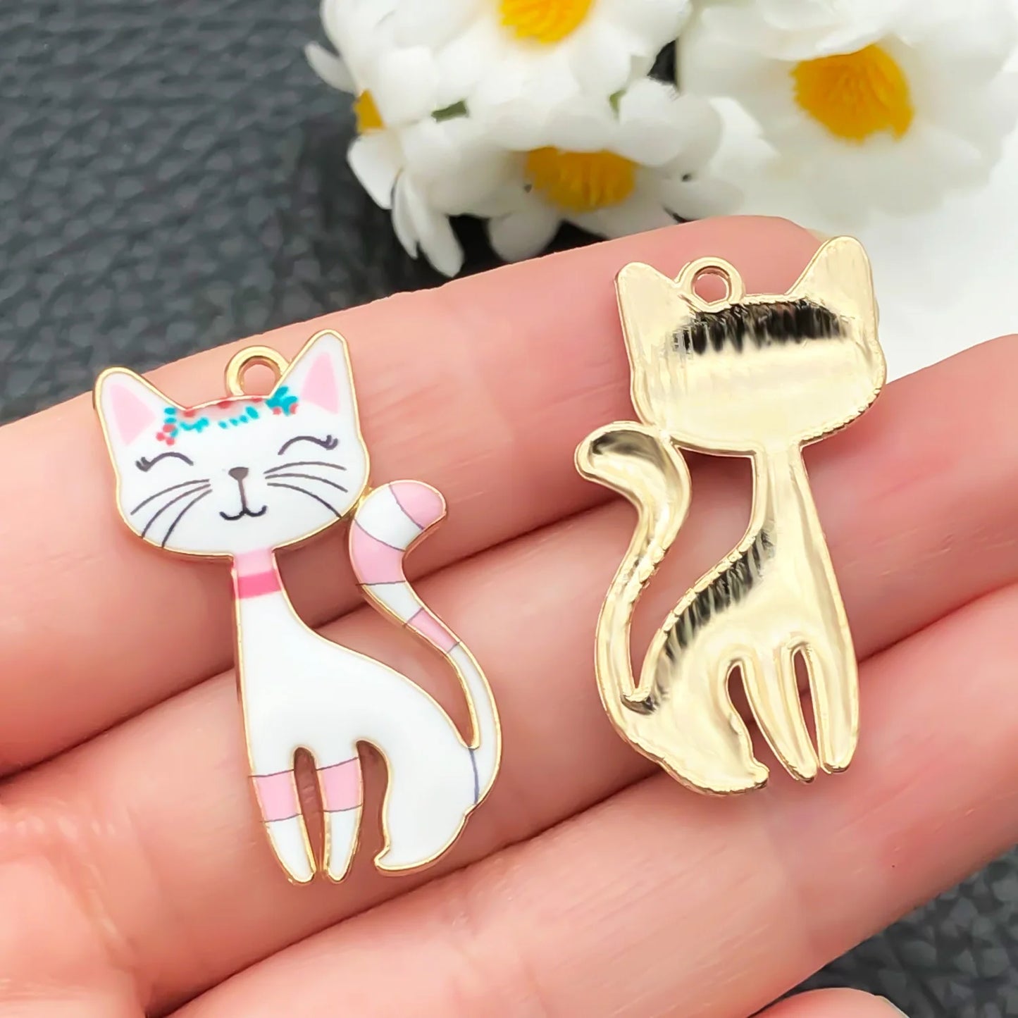 Two cat-shaped charms on a hand with a blurred background of flowers.