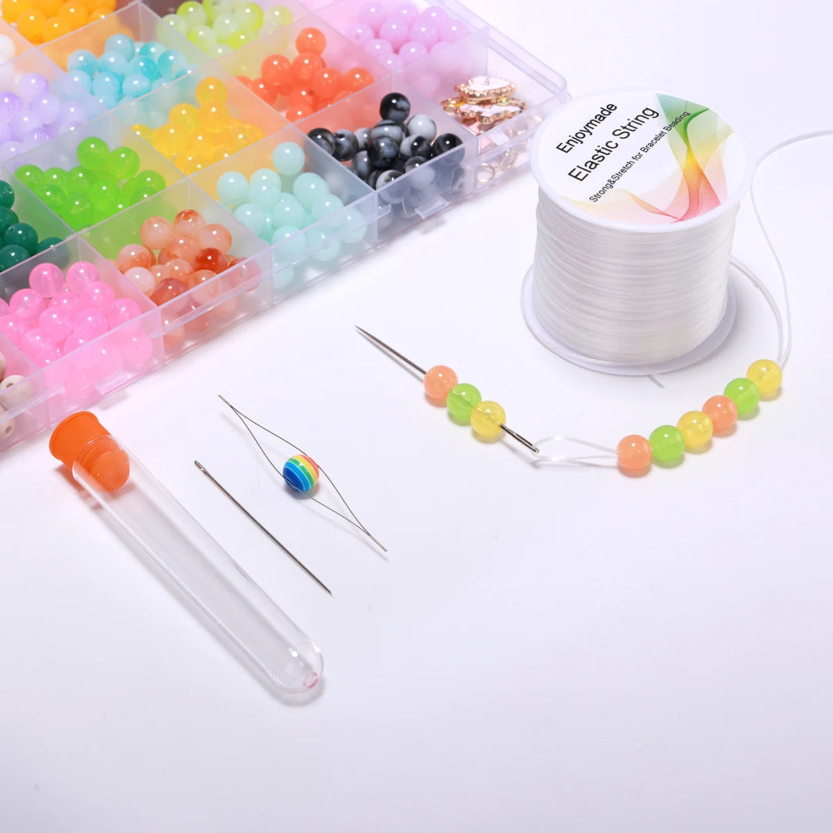 Colorful beads, needles, and a spool of elastic string on a white surface