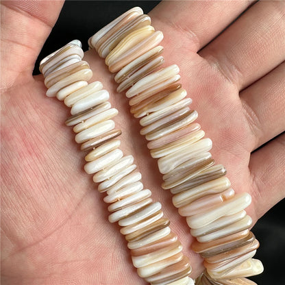 Two strands of mother of pearl shell beads held in a hand against a neutral background