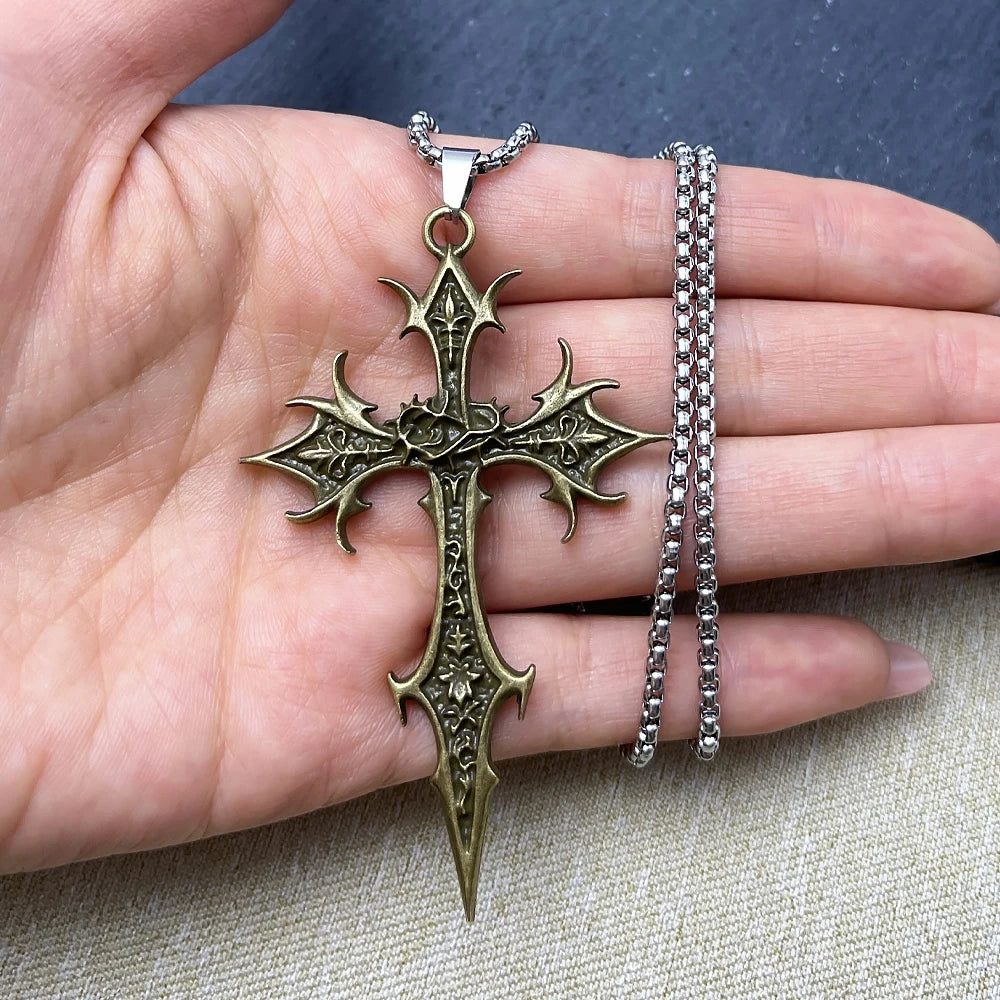 Bronze cross pendant on a chain held in a hand with a neutral background