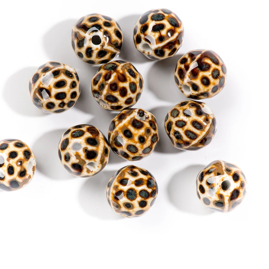 Ten faceted glass beads with a brown and black leopard print pattern on a cream background, arranged on a white surface.