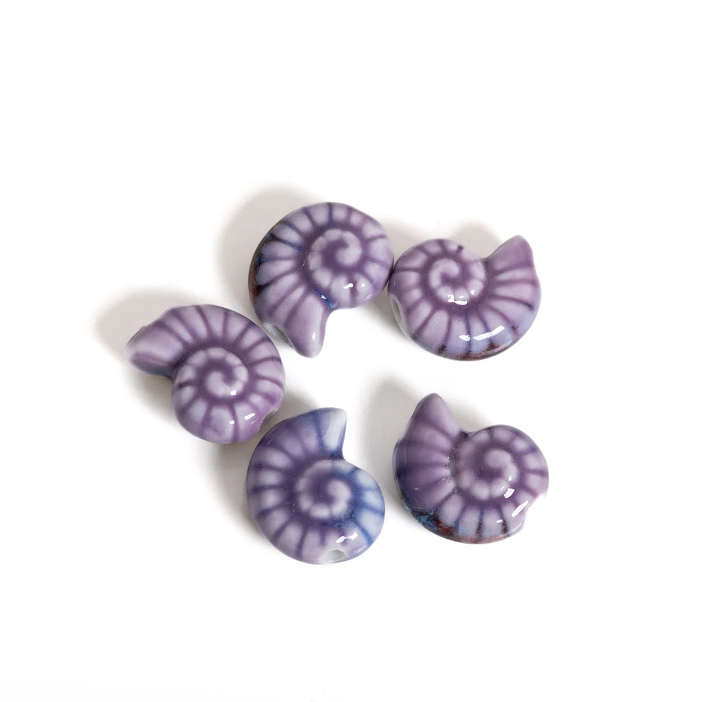 Five small spiral shell-shaped beads in shades of purple and blue with white spiral patterns, arranged on a plain white background.