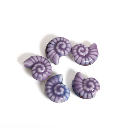 Five small spiral shell-shaped beads in shades of purple and blue with white spiral patterns, arranged on a plain white background.
