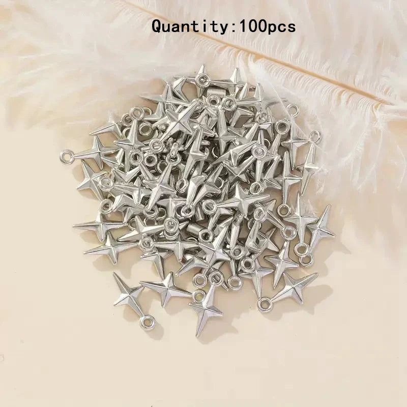 A pile of 100 silver star-shaped jewelry charms with loops, displayed on a light beige surface with white feathers in the background.
