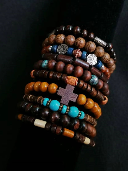 Stack of wooden and beaded bracelets with cross and tree designs on a dark background