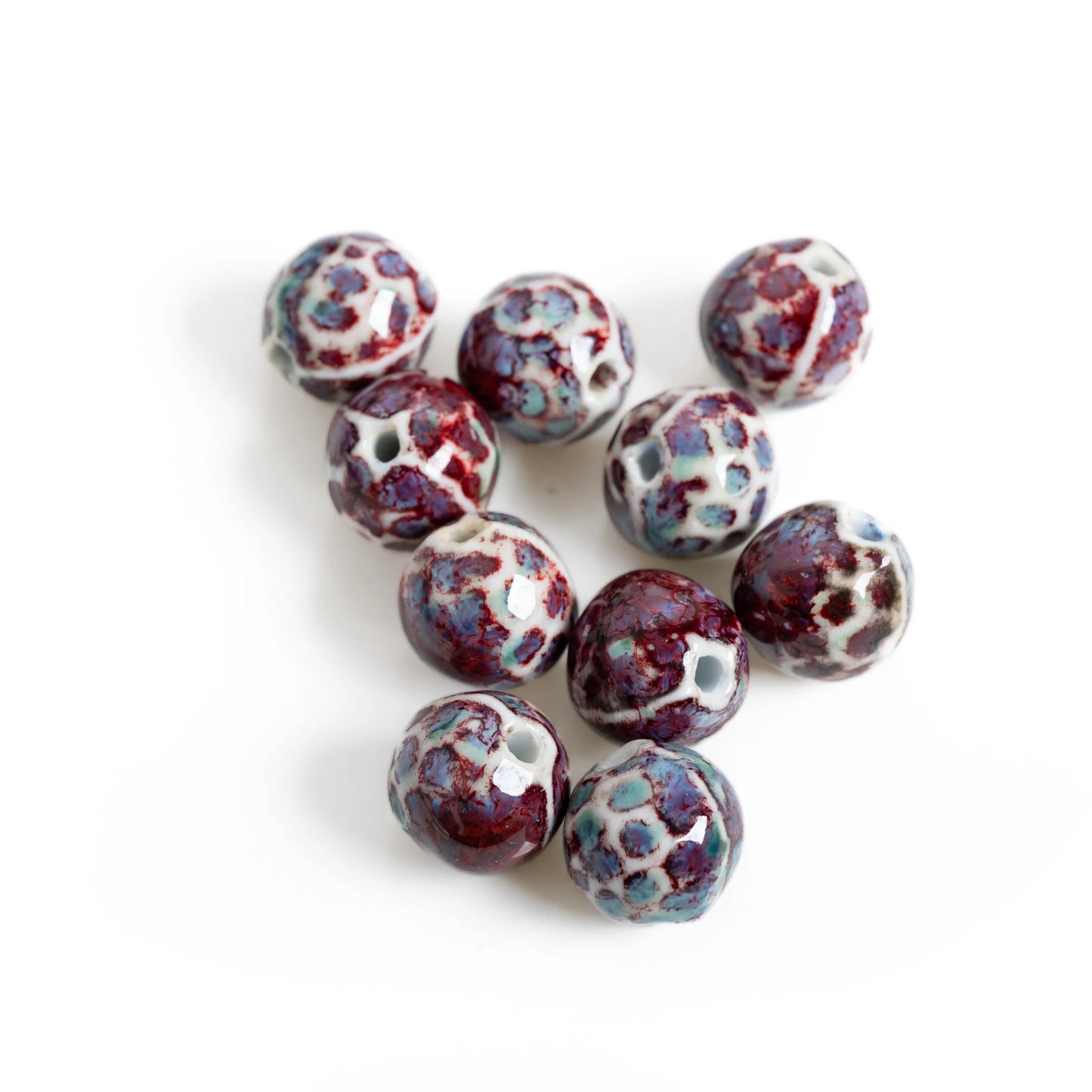Nine round ceramic beads with a mottled glaze of deep burgundy, light blue, and white, arranged on a plain white background.