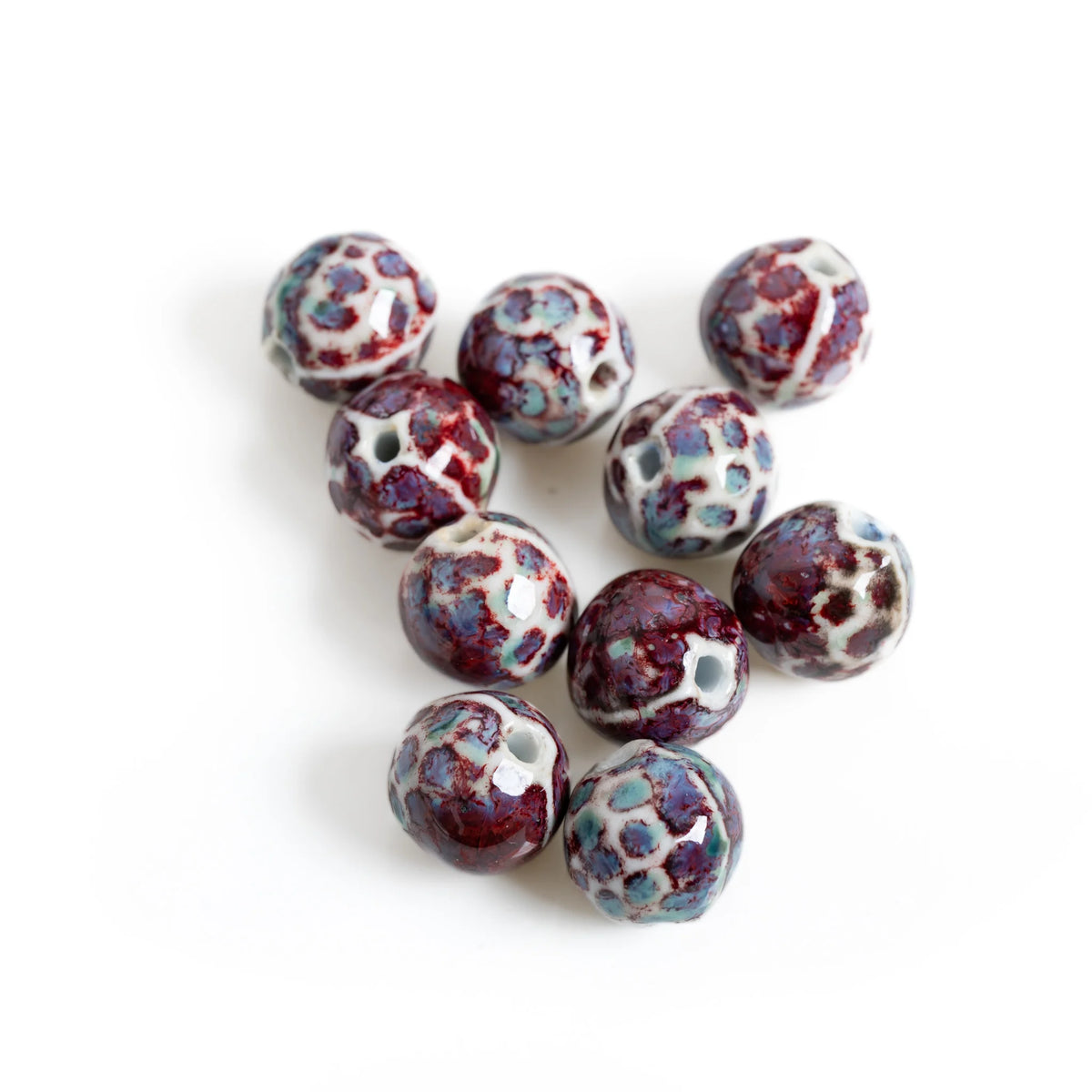 Nine round ceramic beads with a mottled glaze of deep burgundy, light blue, and white, arranged on a plain white background.