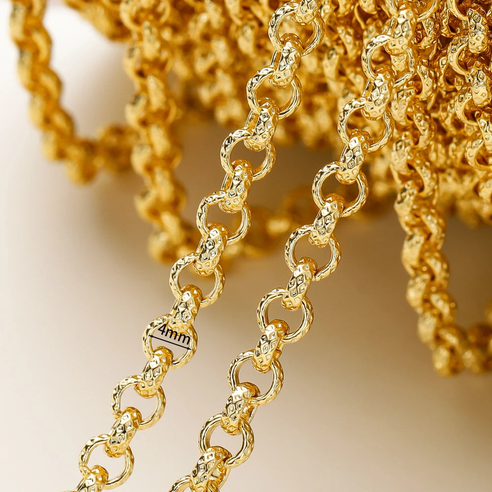 Close-up of a gold chain necklace with textured oval links and a small engraved size marker reading 44mm, shown against a softly blurred warm beige background.