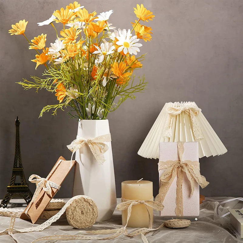 Decorative setting with flowers in a vase, gift box, candle, and lamp on a gray surface.