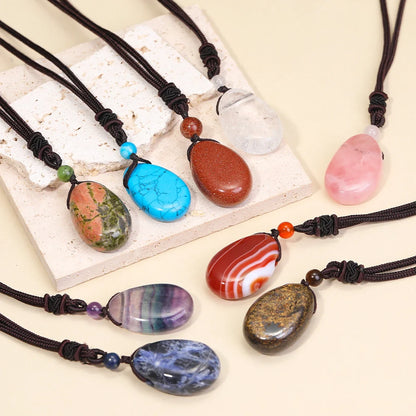 Colorful stone pendants on black cords displayed on a white stone surface.