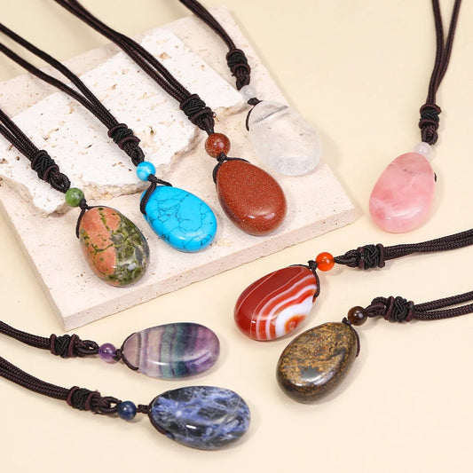 Colorful stone pendants on black cords displayed on a white stone surface.