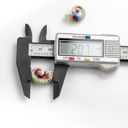 A small multicolored spiral shell is shown under a digital caliper measuring 20.7 mm, with two additional similar shells placed above on a clean white background.