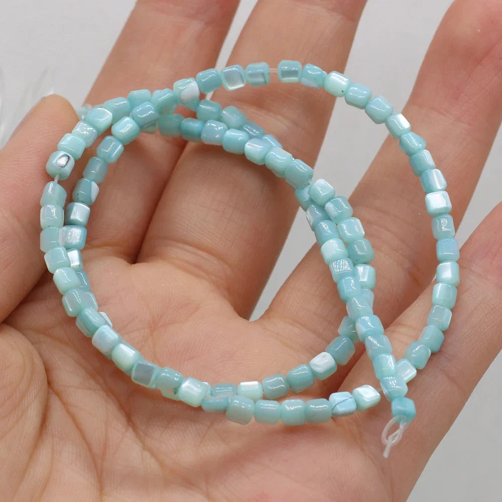 A strand of light blue faceted square shell beads draped over an open hand, showing the texture and color of the beads against the skin.