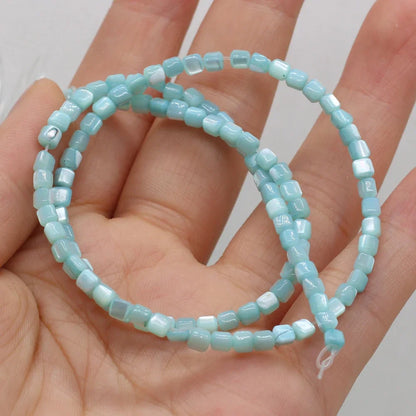 A strand of light blue faceted square shell beads draped over an open hand, showing the texture and color of the beads against the skin.