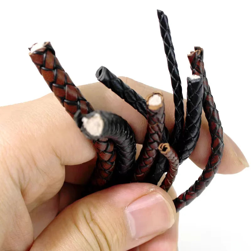 A hand holding several braided leather cords in black and reddish-brown tones against a plain white background.
