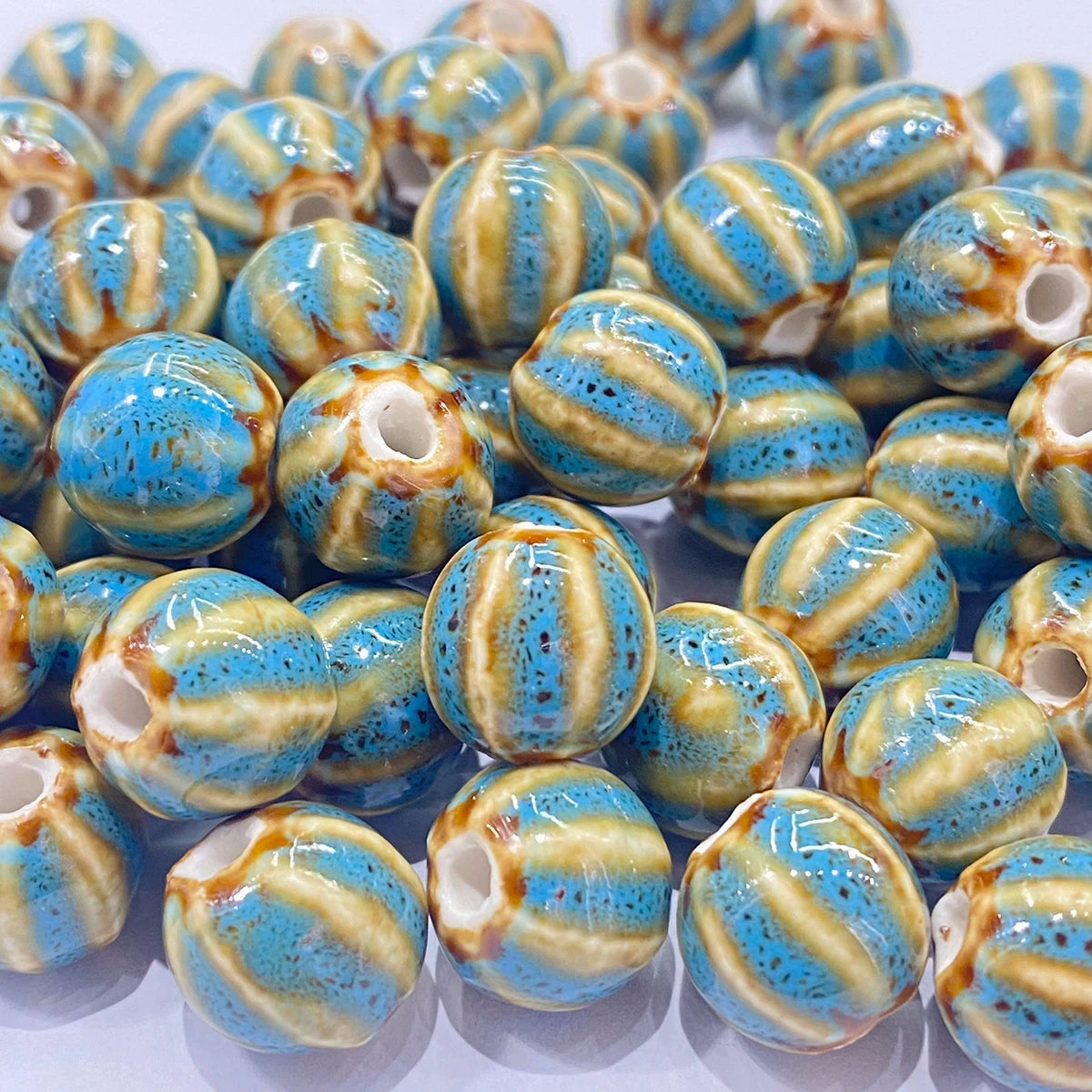 A pile of round ceramic beads with a glossy finish, featuring a mottled blue and beige striped pattern with small brown speckles and a central hole.