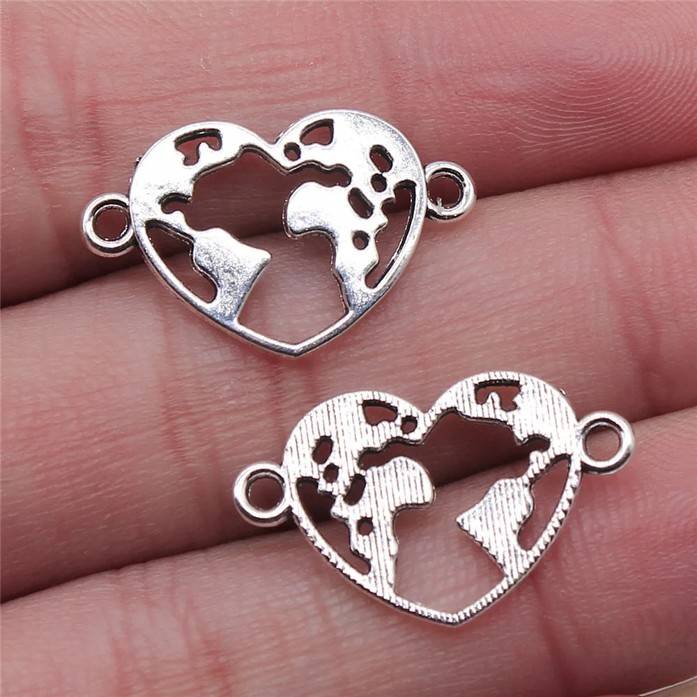 Two silver heart-shaped world map pendants on a hand.