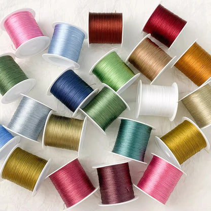 A collection of colorful embroidery thread spools arranged on a white textured background. The threads come in a variety of colors including pink, blue, green, red, brown, gold, white, and purple.