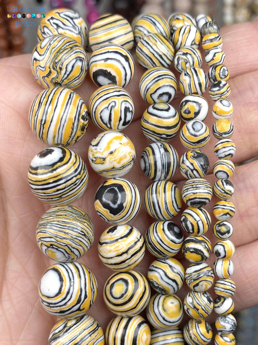 A close-up of multiple strands of round beads held in a hand. The beads have a glossy finish and feature a marbled swirl pattern of yellow, black, white, and gray.