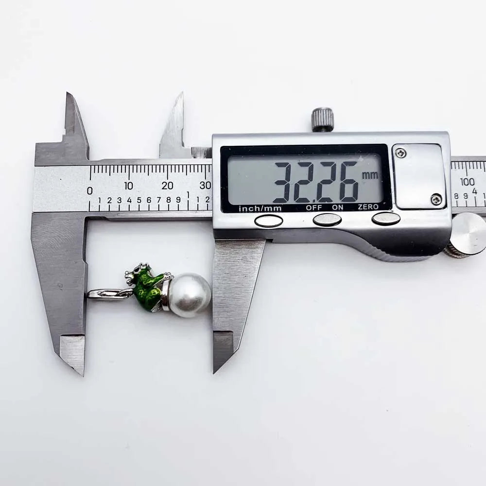 Digital caliper measuring a green gemstone and pearl on a white background