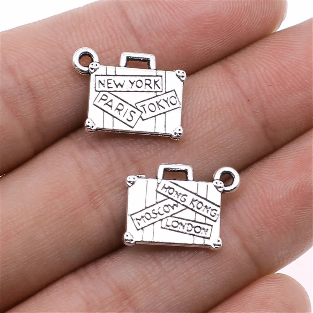 Silver charm shaped like a suitcase with city names on it, held between fingers.