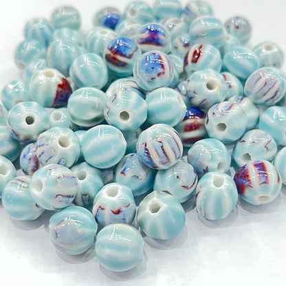 A pile of round glass lampwork beads with a glossy finish, featuring a light blue and white marbled pattern with accents of dark blue and reddish-brown swirls.