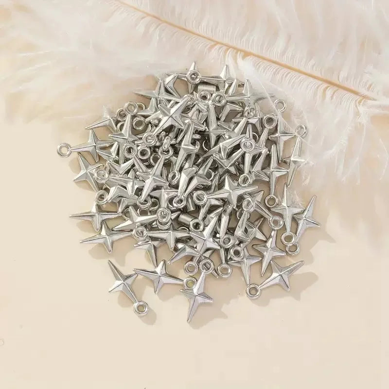 A pile of silver-toned metal shuriken star charms with hanging loops, arranged on a light beige surface with white feathers in the background.